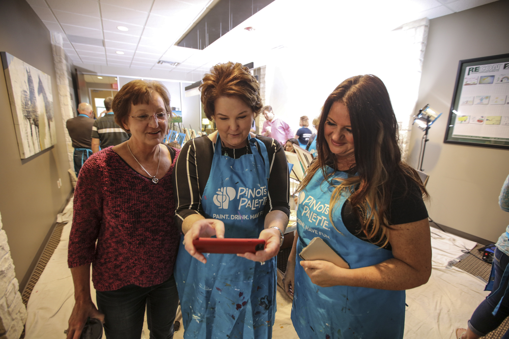 three women in aprons looking at phone together